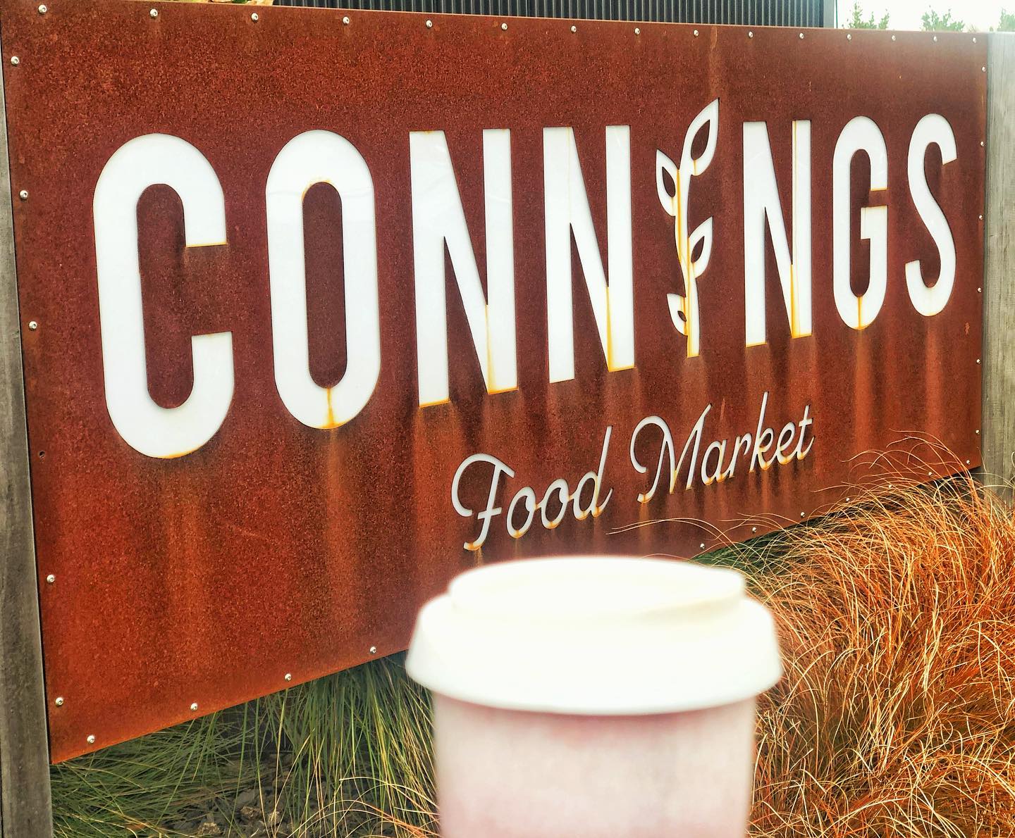 The rust-coloured Connings Food Market sign with a takeaway coffee in front