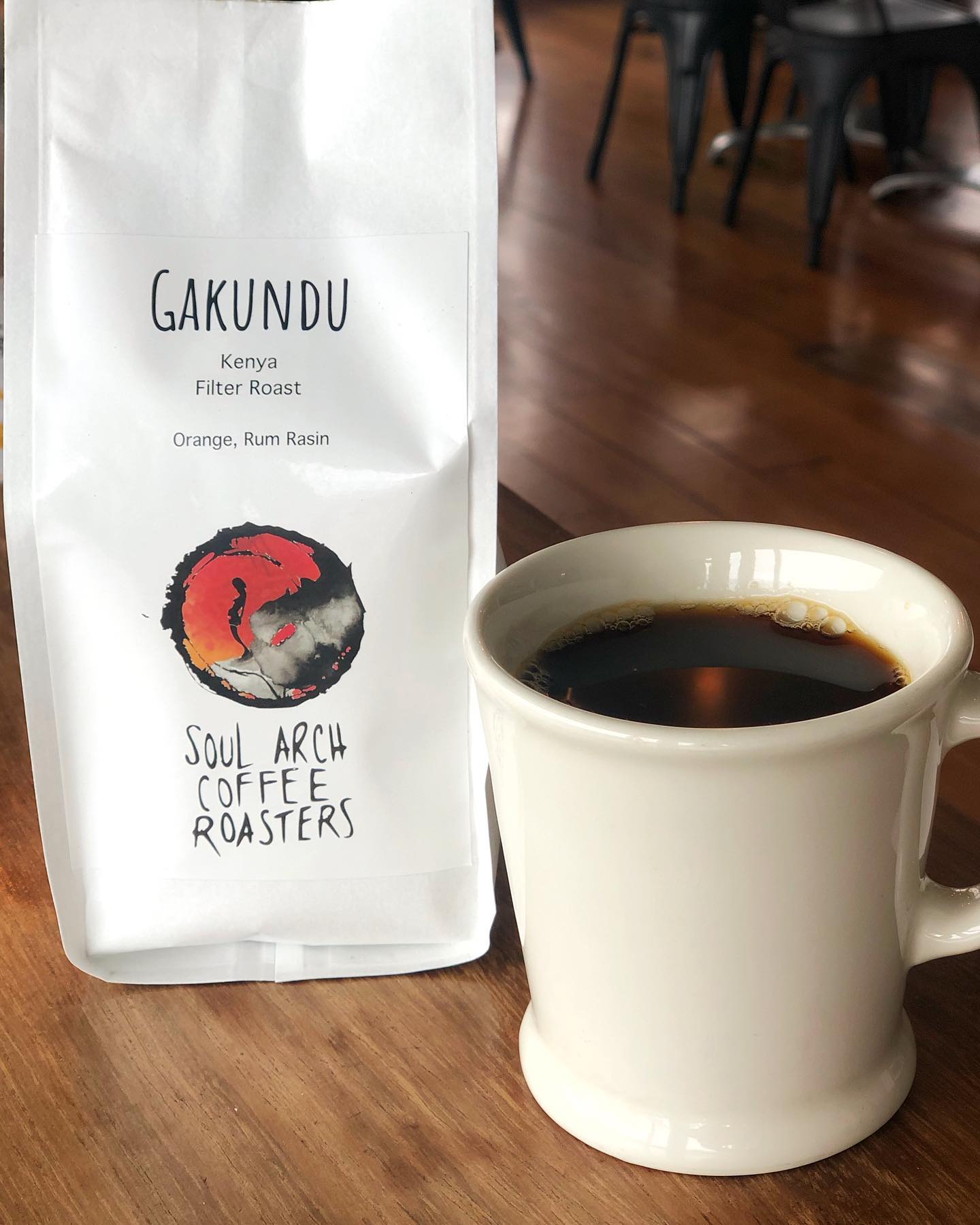 A Gakundu Kenya filter roast bag with a red ink logo beside a white mug of black coffee